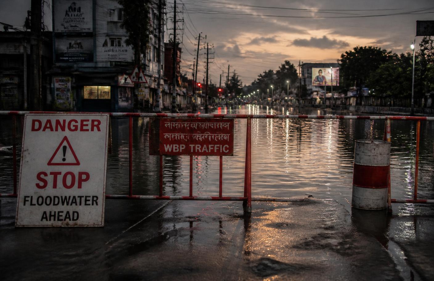 A barricaded flooded street at dusk with a danger warning sign